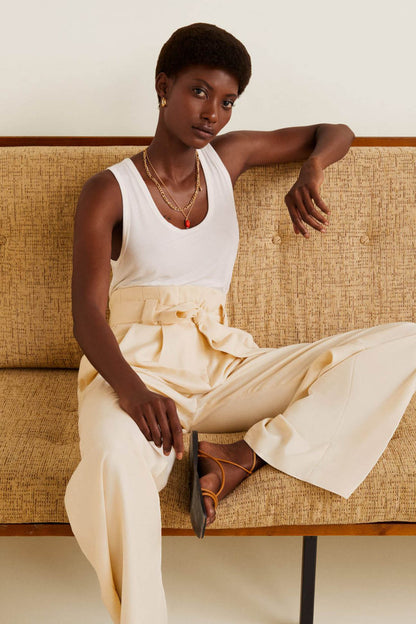 Off-white wide-leg pants with tie belt and sleeveless tank top, seated pose