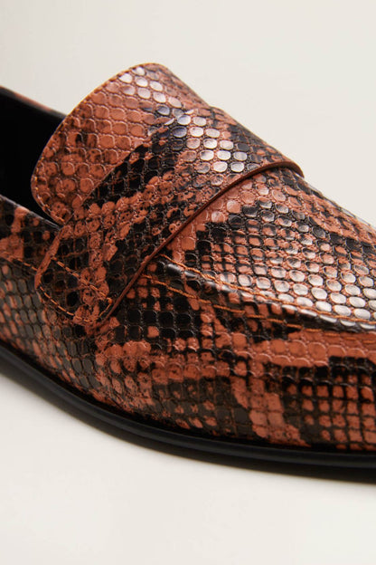 Close-up of orange-brown snake-print loafer with black seam and black sole