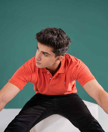 Orange fitted polo shirt with short sleeves and chest logo, model leaning forward