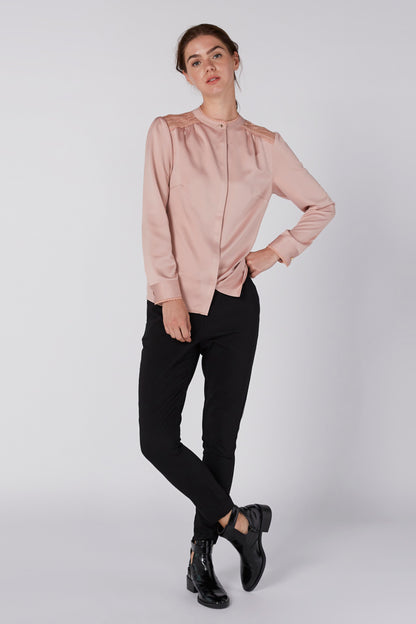Light pink zip-front blouse with long sleeves and stand collar, worn with black pants