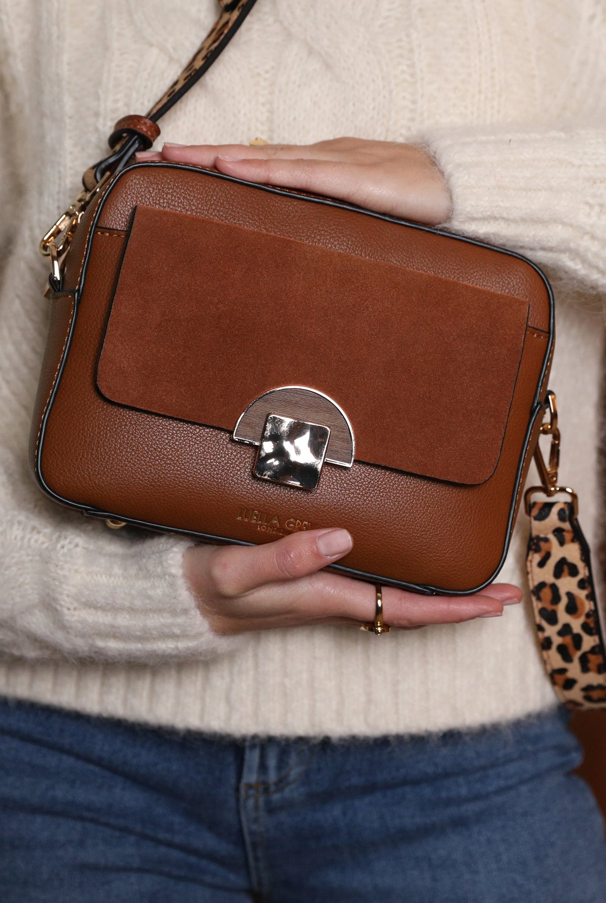 Brown leather crossbody bag in hand with flap, silver turn-lock, and leopard strap