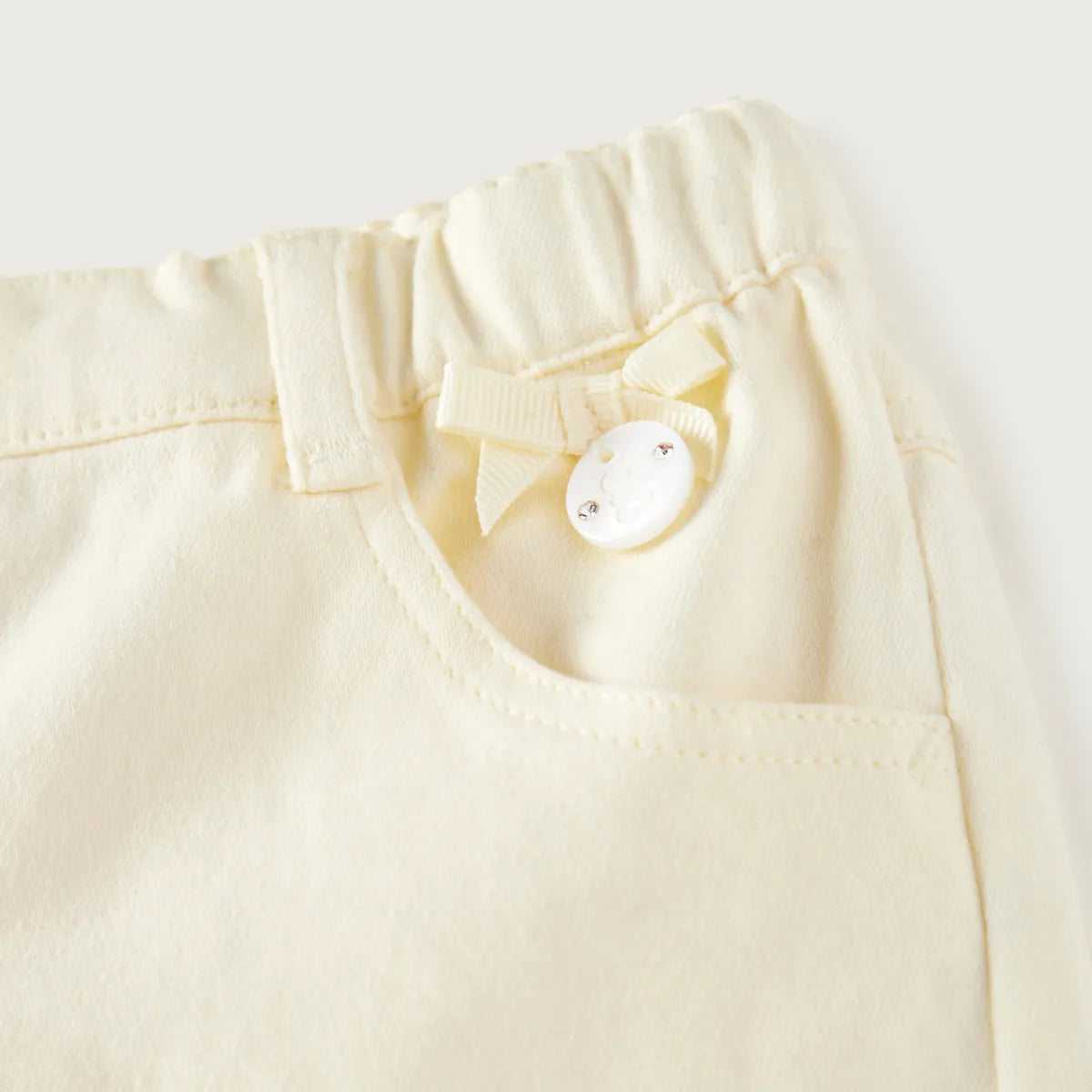Pale yellow baby pants close-up: elastic waist with bow and snap button