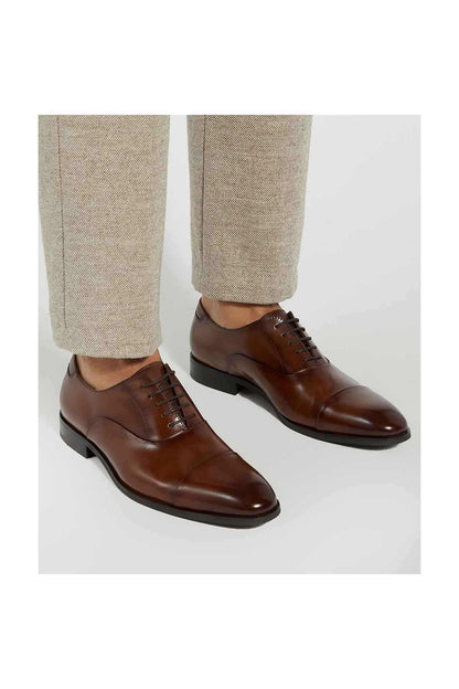 Pair of dark tan lace-up oxford shoes worn with light trousers