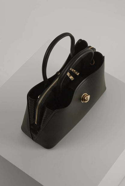 Black handbag side view with top handles, gold zipper pocket, and front turn-lock clasp