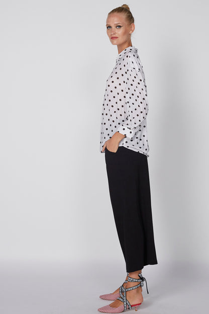 White polka-dot button-up shirt with collar, side view with black trousers