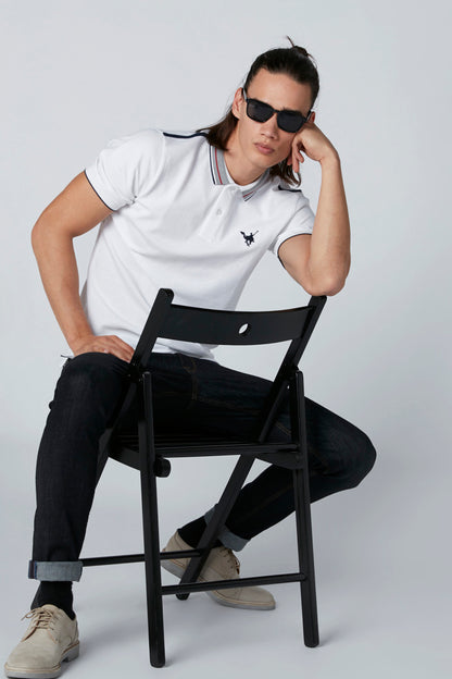 White polo shirt with striped collar and small chest logo, paired with dark jeans