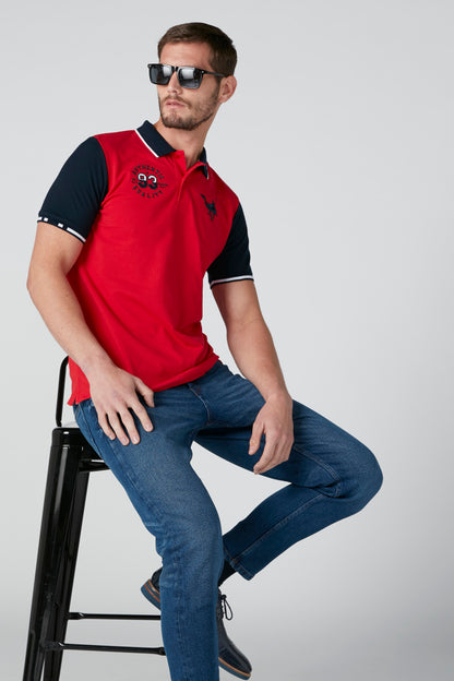 Red polo shirt with dark navy sleeves and chest graphic, paired with blue jeans