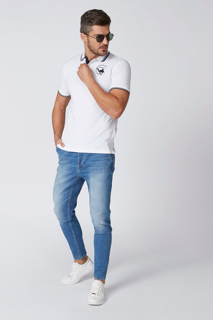 White polo shirt with navy trim collar, chest logo, worn over blue jeans
