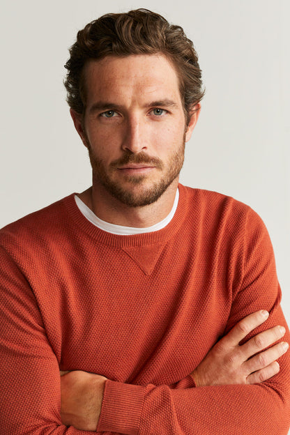 Men's rust-orange crewneck sweater with ribbed cuffs, arms crossed