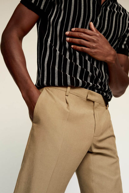 Tan chino trousers with pleats, side pockets, and button fly detail