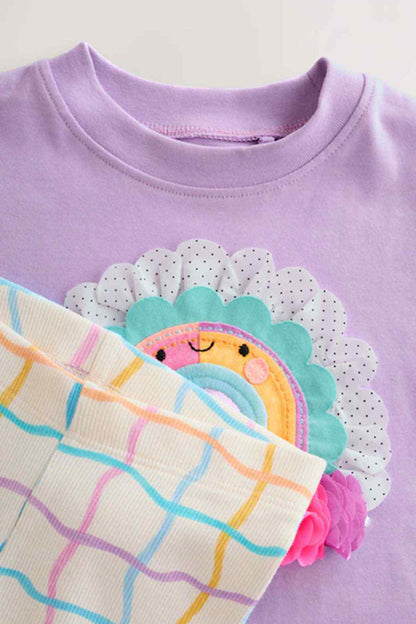 Close-up of lilac T-shirt hem with rainbow applique and white leggings with colorful grid print