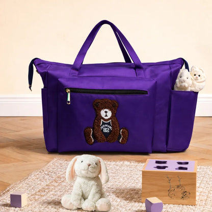 Purple tote bag with teddy patch and plush items in side compartment