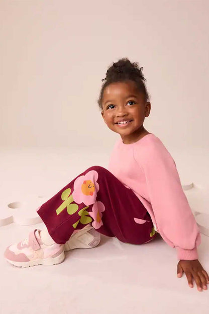 Kids burgundy floral pants with elastic waistband, sitting pose