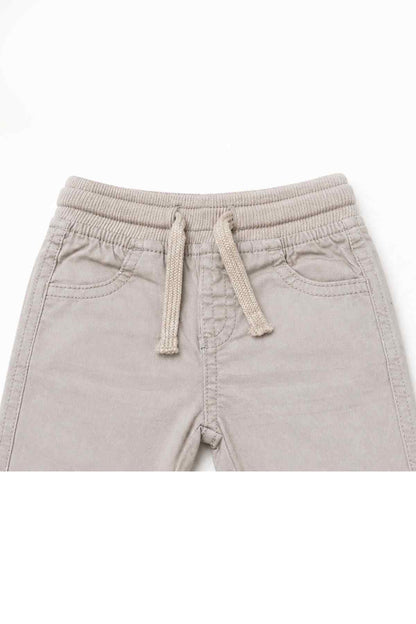 Beige baby pants waistband with elastic, front drawstring tie, and stitched pocket details