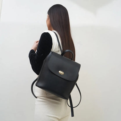Black flap handbag with gold-tone emblem, adjustable shoulder straps and drawcord ties