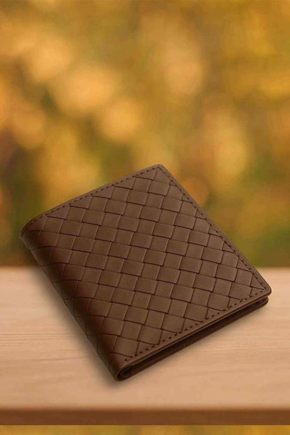Brown leather bifold wallet with woven check pattern, angled on tabletop