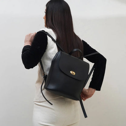 Black shoulder handbag with front flap and gold-tone emblem, long strap with ties