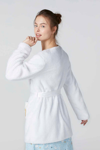 White plush bathrobe with tie belt, long sleeves, and embroidered patches at hem