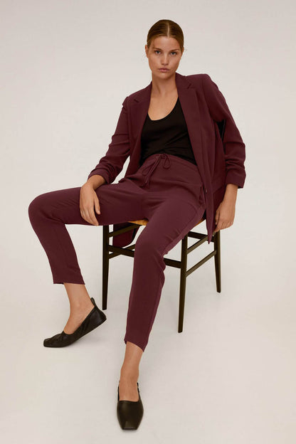 Maroon women's blazer with matching tapered trousers, seated front pose