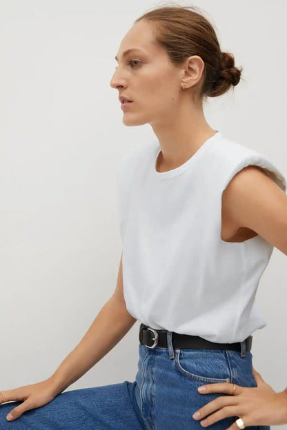 White sleeveless crewneck top with blue jeans and black belt, profile with hands on hip