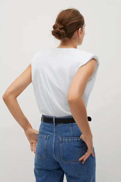 White sleeveless top with open back, blue jeans with black belt, back view