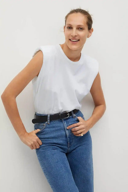 White sleeveless crewneck top tucked into blue jeans with black belt, hands on hips