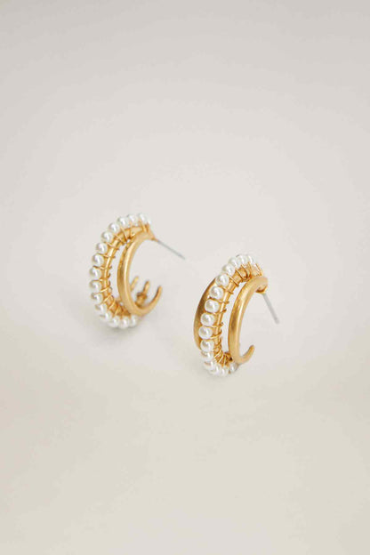 Gold hoop earrings with pearl beads and prong-like detailing, close-up