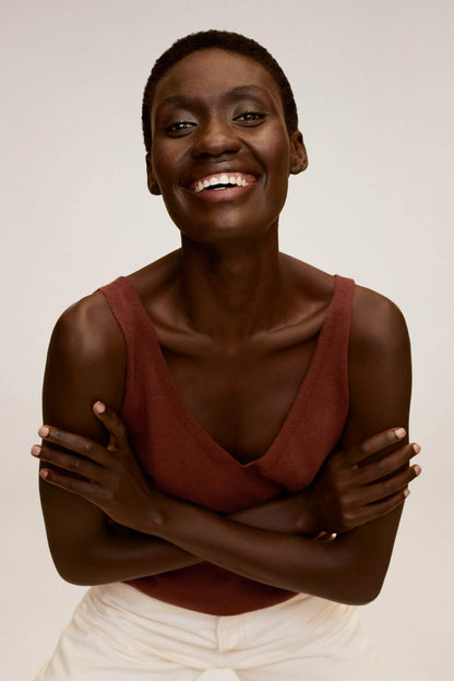 Brown V-neck sleeveless top with draped front, arms crossed