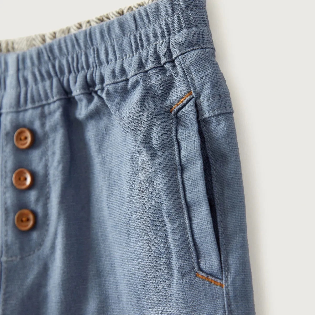 Blue baby pants close-up: elastic waistband with brown buttons and side pocket