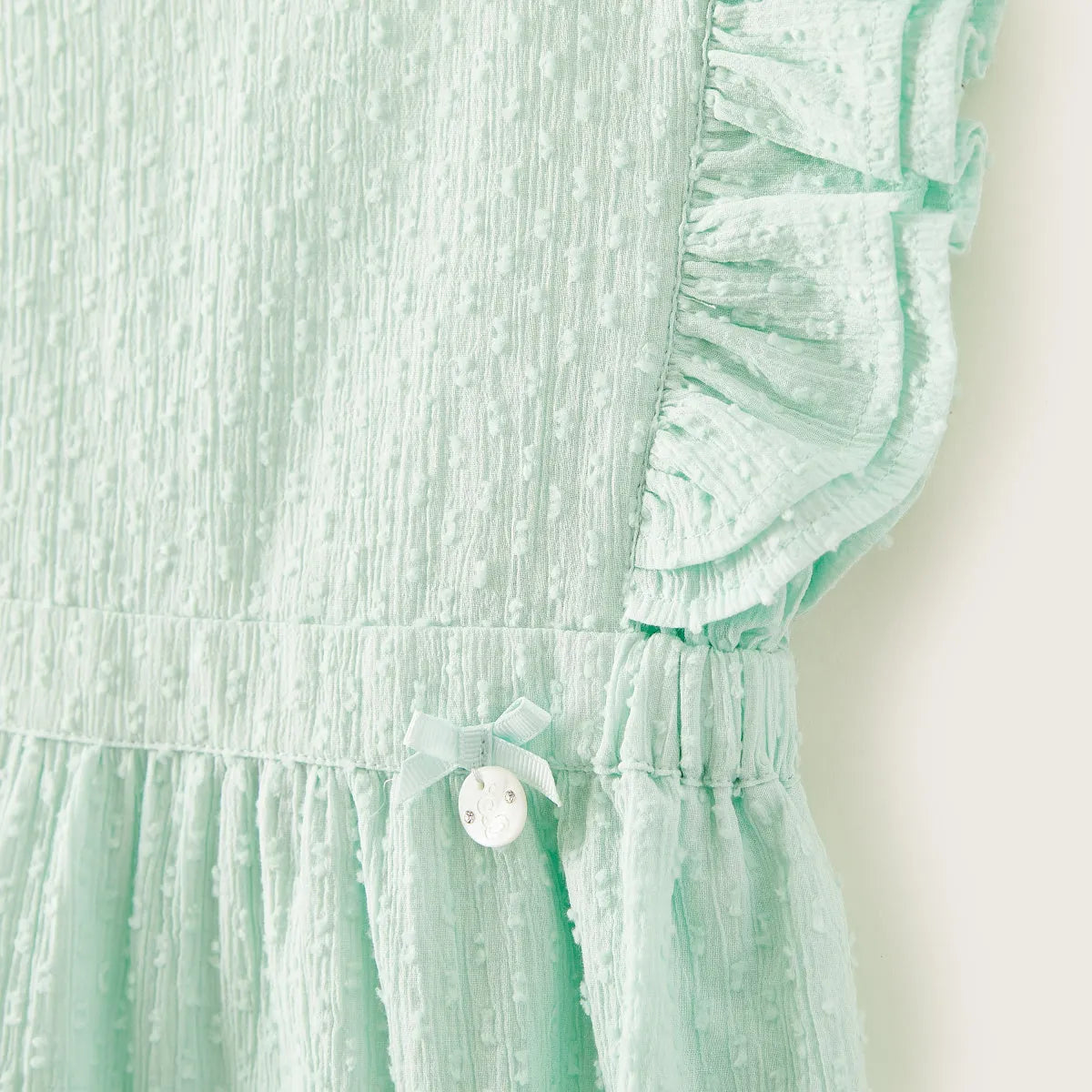 Mint green baby dress close-up: ruffled sleeve, pleated bodice, and round front button