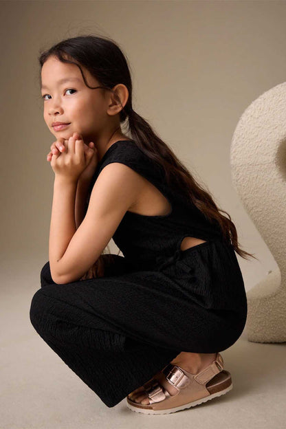 Kids black sleeveless jumpsuit with tie waist and cutout back detail