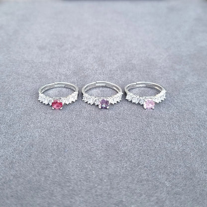 Three silver-tone rings with fringe details and pink and purple center gemstones