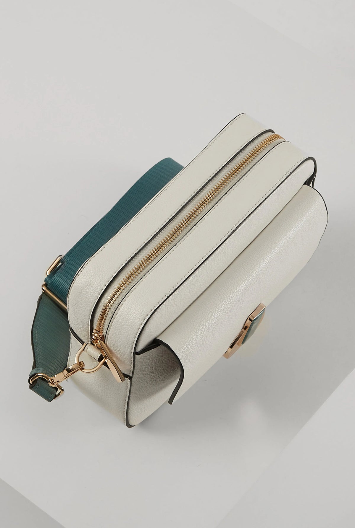 White shoulder bag with teal strap, curved flap, gold zipper trim and top opening