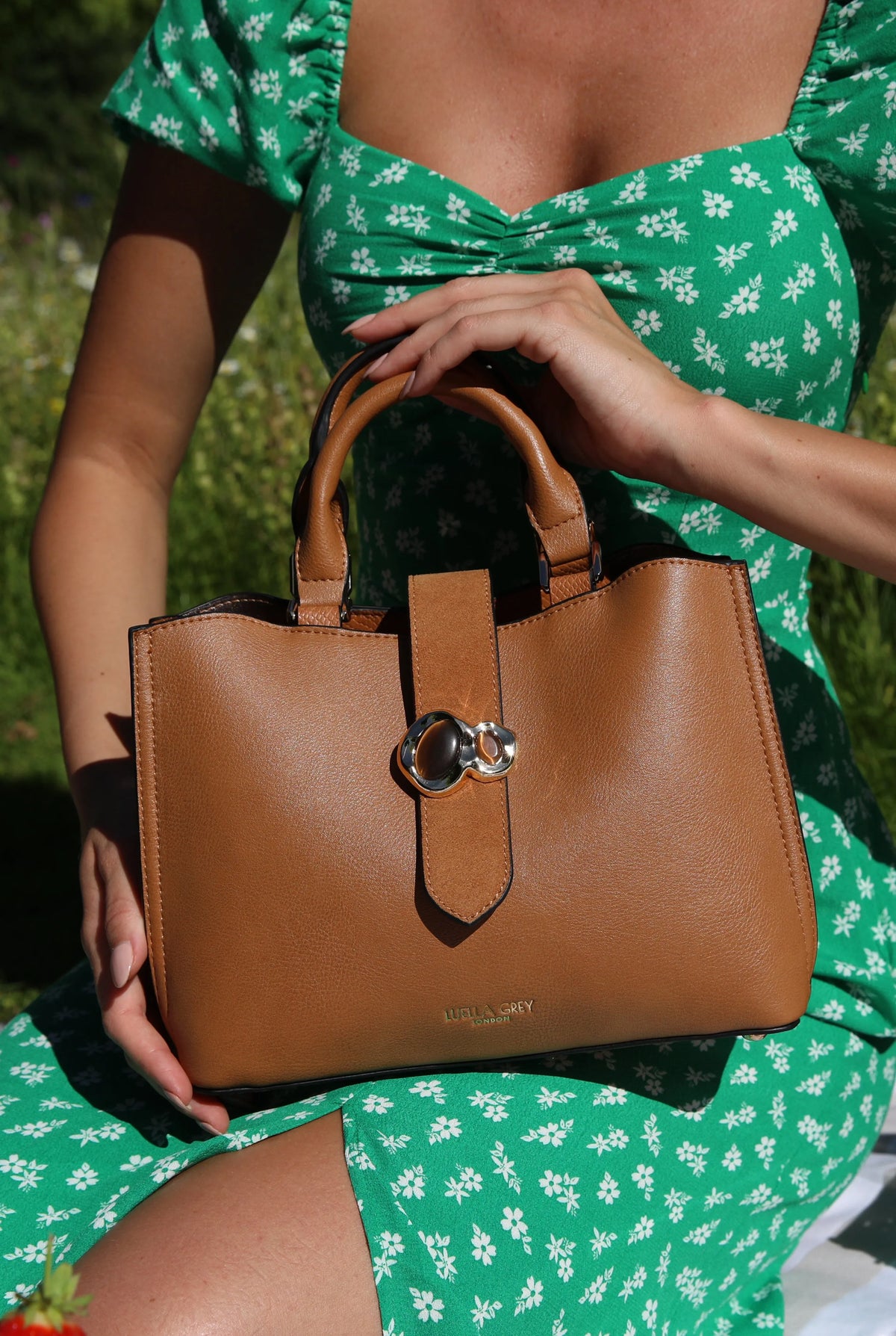 Luella Grey brown handbag held in hand with front strap and metal clasp