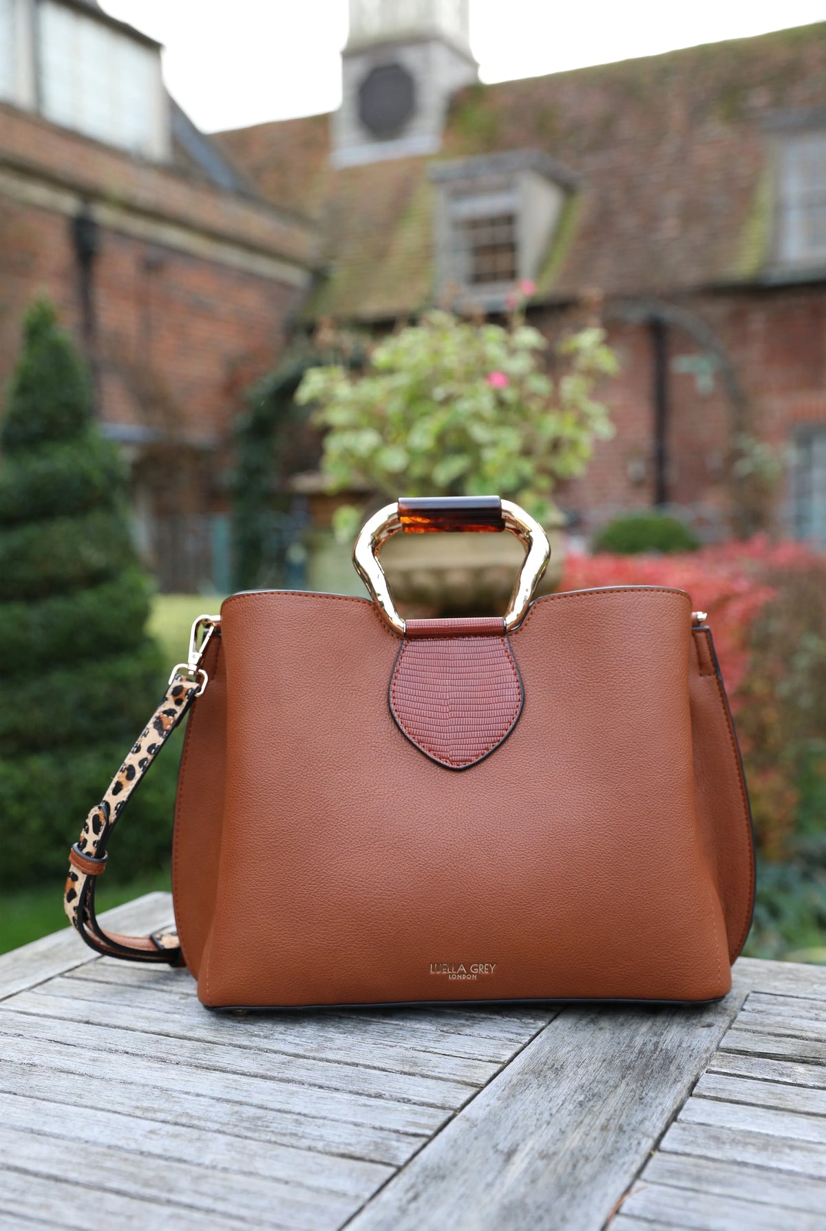 Brown tote-style handbag with metal top clasp and long crossbody strap