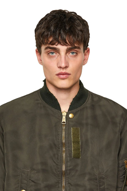 Olive bomber jacket close-up with gold zipper pull and chest patch pocket