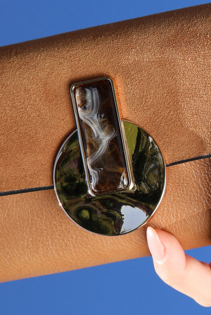Brown leather wallet detail with round metal clasp and patterned button
