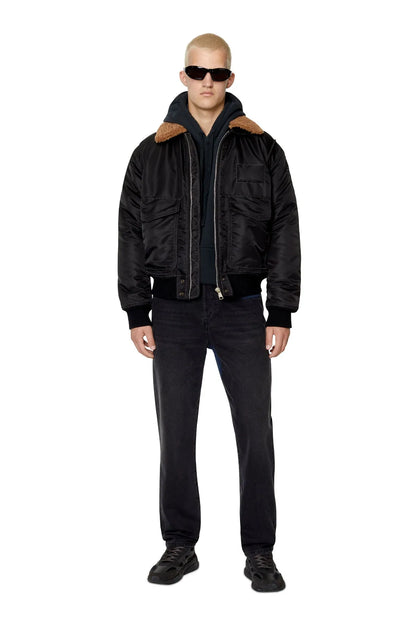 Men's black bomber jacket with tan shearling collar, zip front, and dark jeans