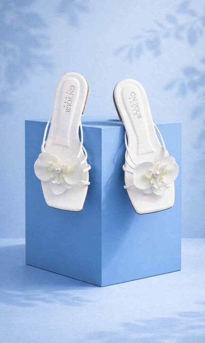 White slide sandals with white flower detail on the toe, on blue boxes