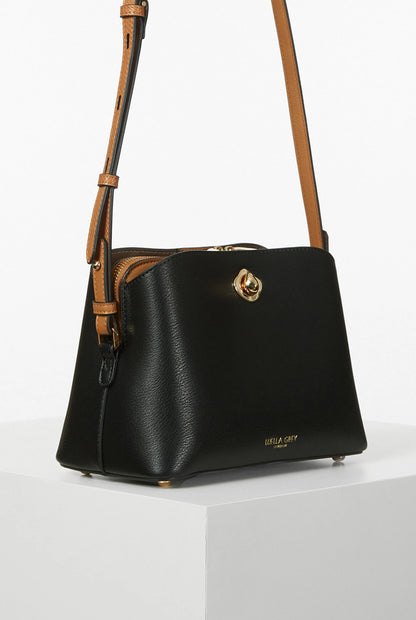 Black mini crossbody bag, side view, gold clasp center and tan-trim edges
