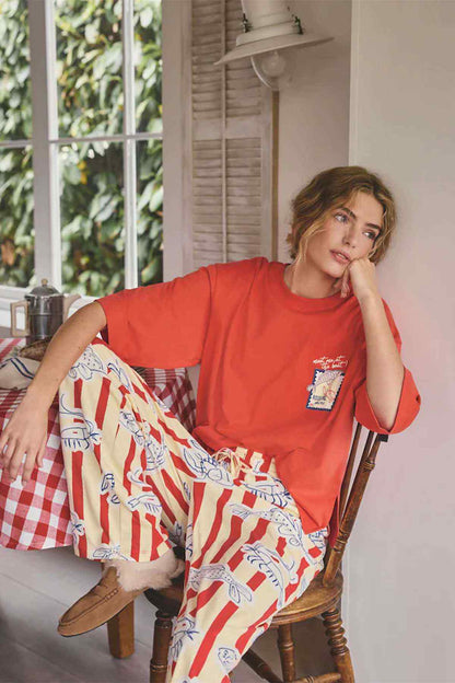 Red T-shirt with chest logo graphic and striped pajama pants, seated