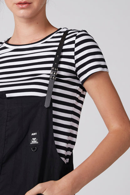 Black bib pinafore with pocket and metal strap detail over striped T-shirt