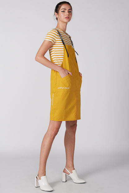 Yellow pinafore overalls with black straps over striped short-sleeve T-shirt