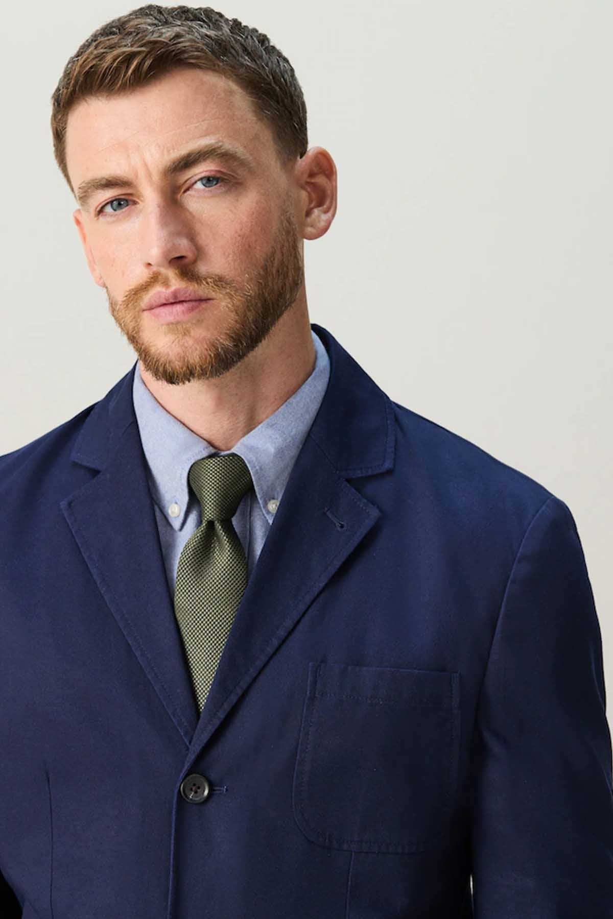 Navy men's suit jacket with green patterned tie and collared shirt