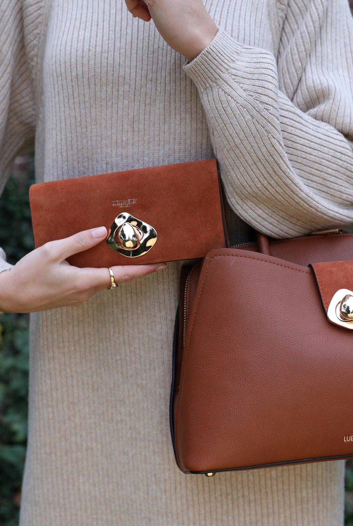 Brown foldover wallet with circular metal clasp, shown in hand