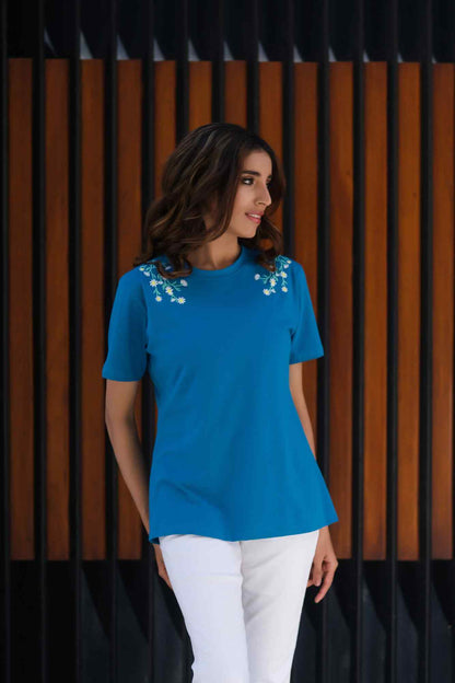 Blue short-sleeve blouse with floral shoulder details; worn with white pants