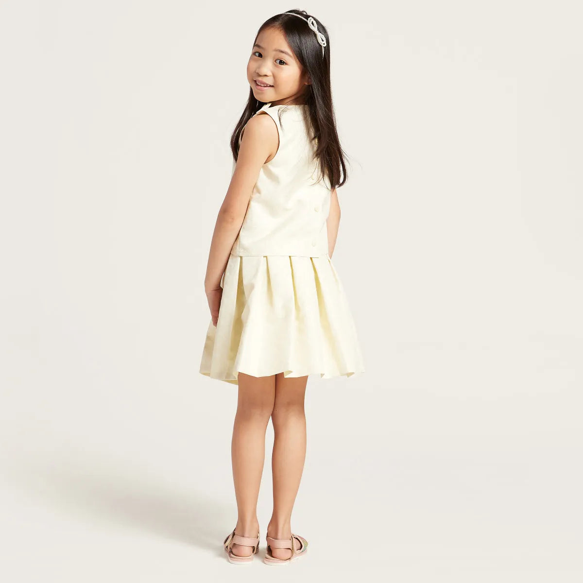 Sleeveless cream bodice with light yellow pleated skirt and round neck