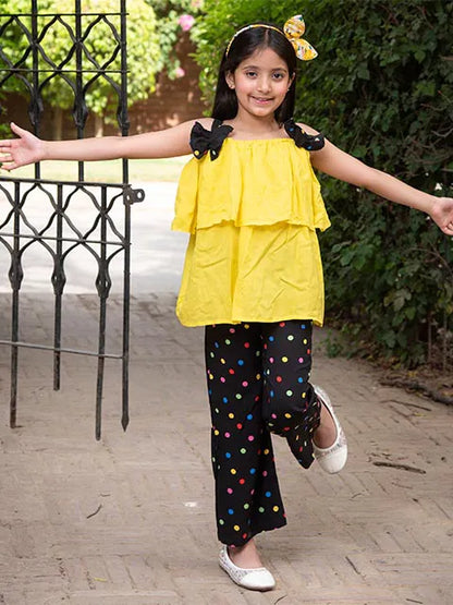 Girls yellow ruffle sleeveless top with black polka-dot pants and bow accents, arms out