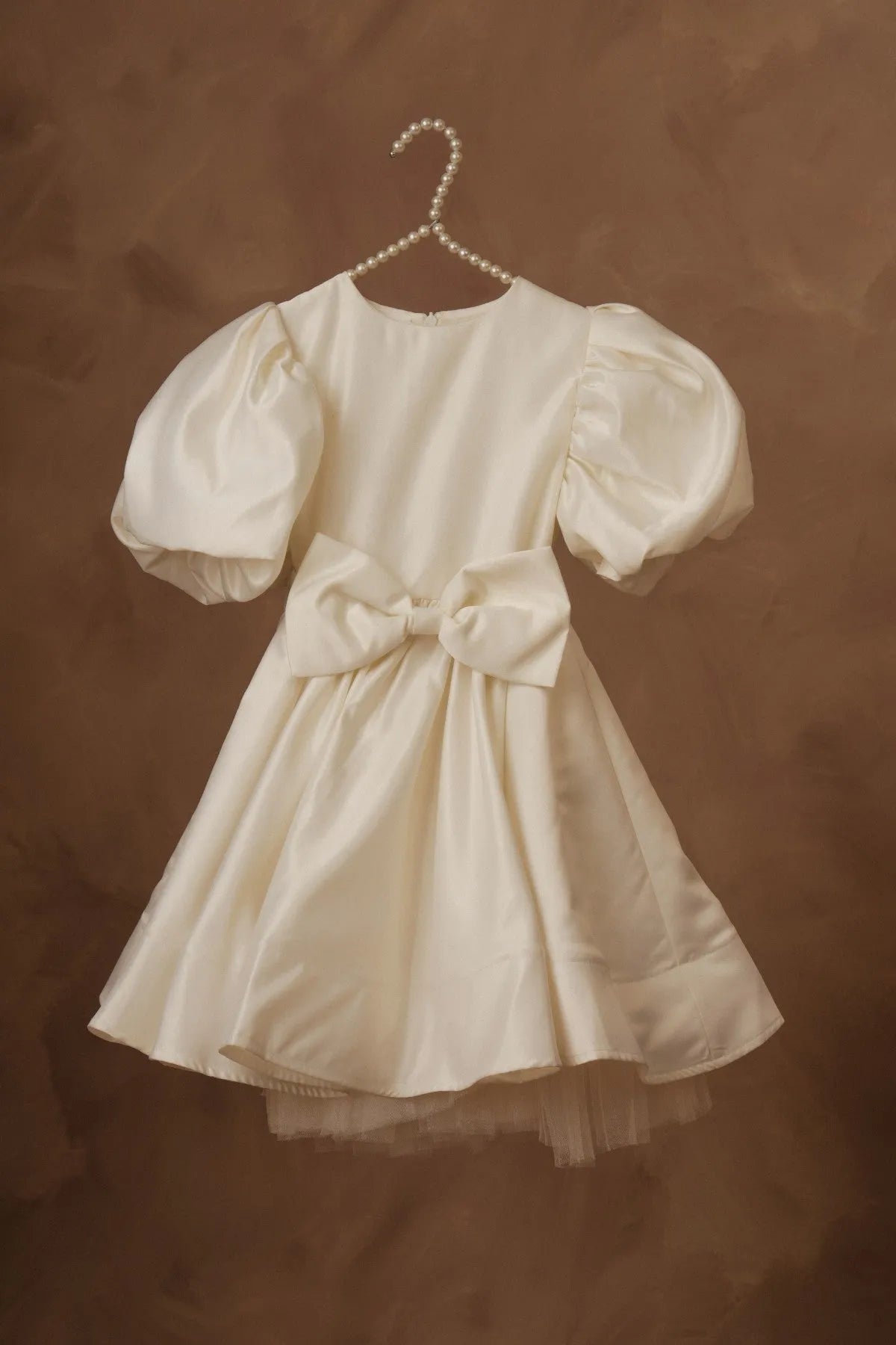White puff-sleeve dress on hanger with waist bow and layered tulle hem