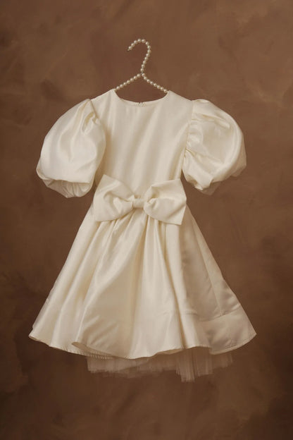 White puff-sleeve dress on hanger with waist bow and layered tulle hem